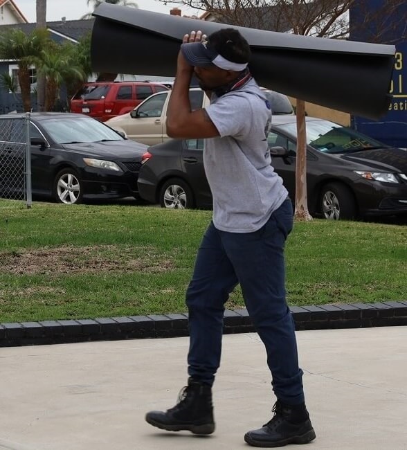 American Van Lines Delivery crew member Mover carries a rolled mat across a driveway during long-distance moving prep.