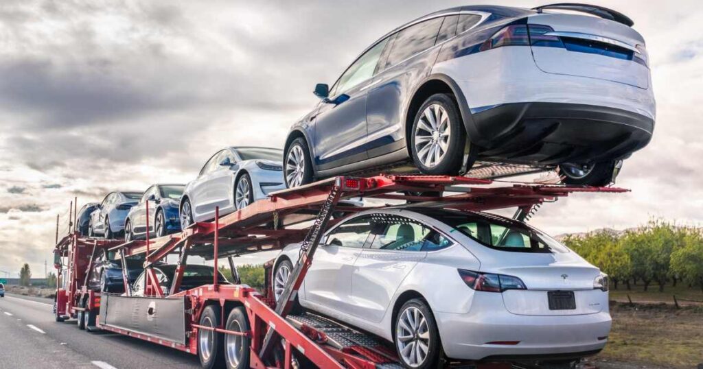 Open car carrier transporting multiple vehicles on a highway — car shipping service during long-distance relocation.